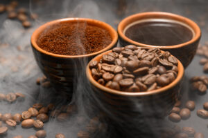 Cups of coffee among selected and calibrated Arabica coffee beans scattered on a black background.